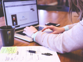 Person at computer with phone and notebook.